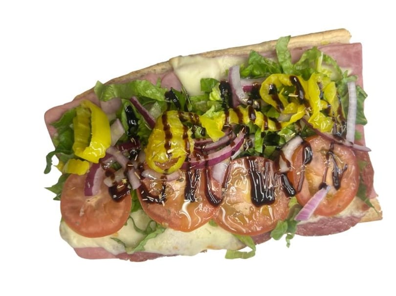 Close-up of a loaded Italian sub with meats, cheese, lettuce, tomatoes, onions, and peppers.