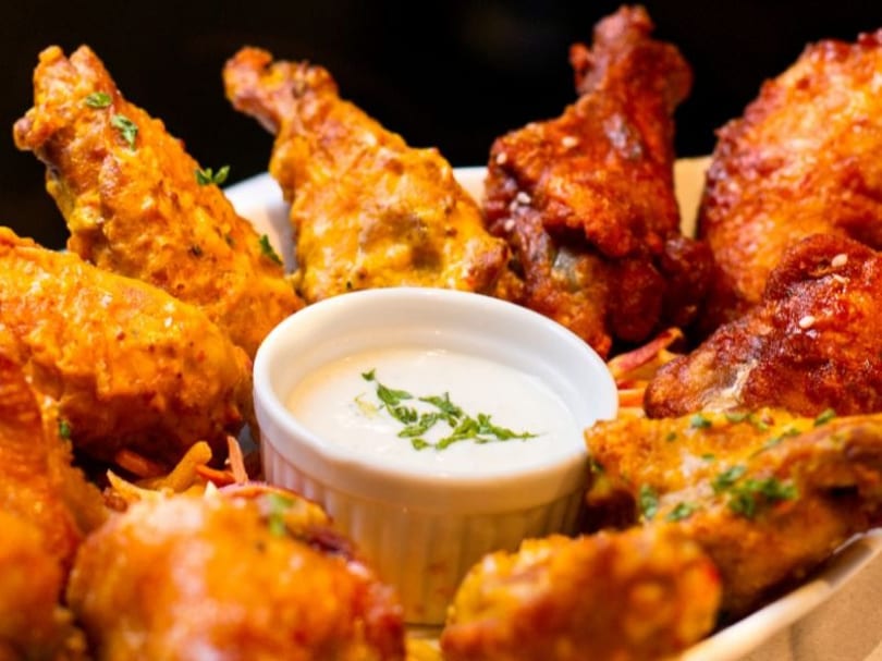 A platter of various chicken wings, some spicy red and some golden, with a side of white dipping sauce.
